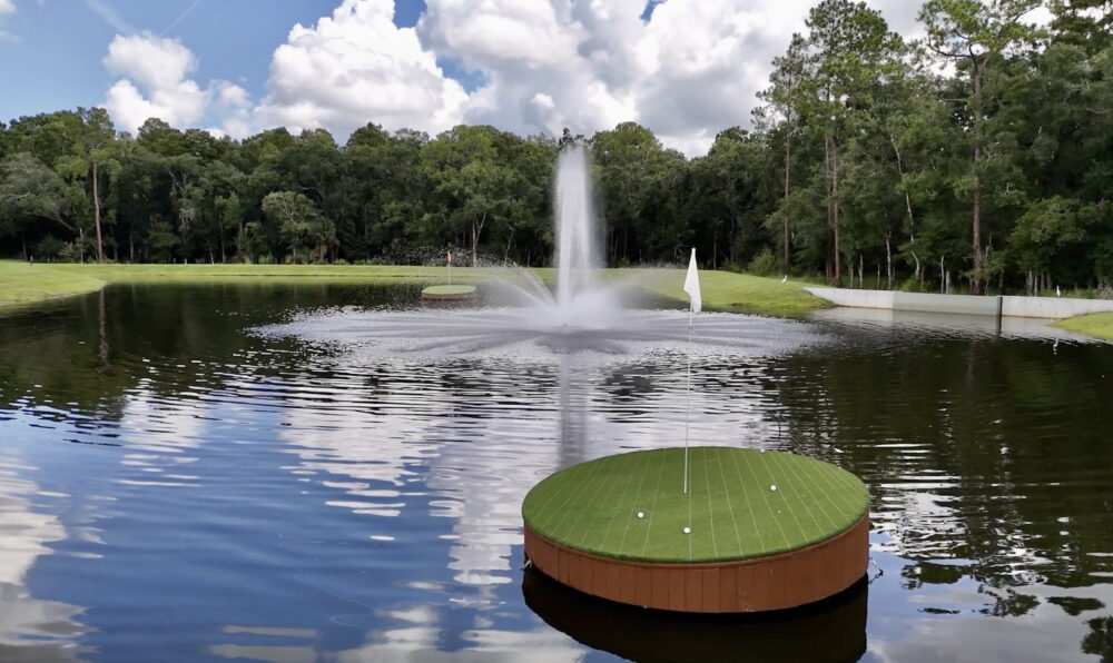 Golf green floating in a pond with a sprinkler behind it