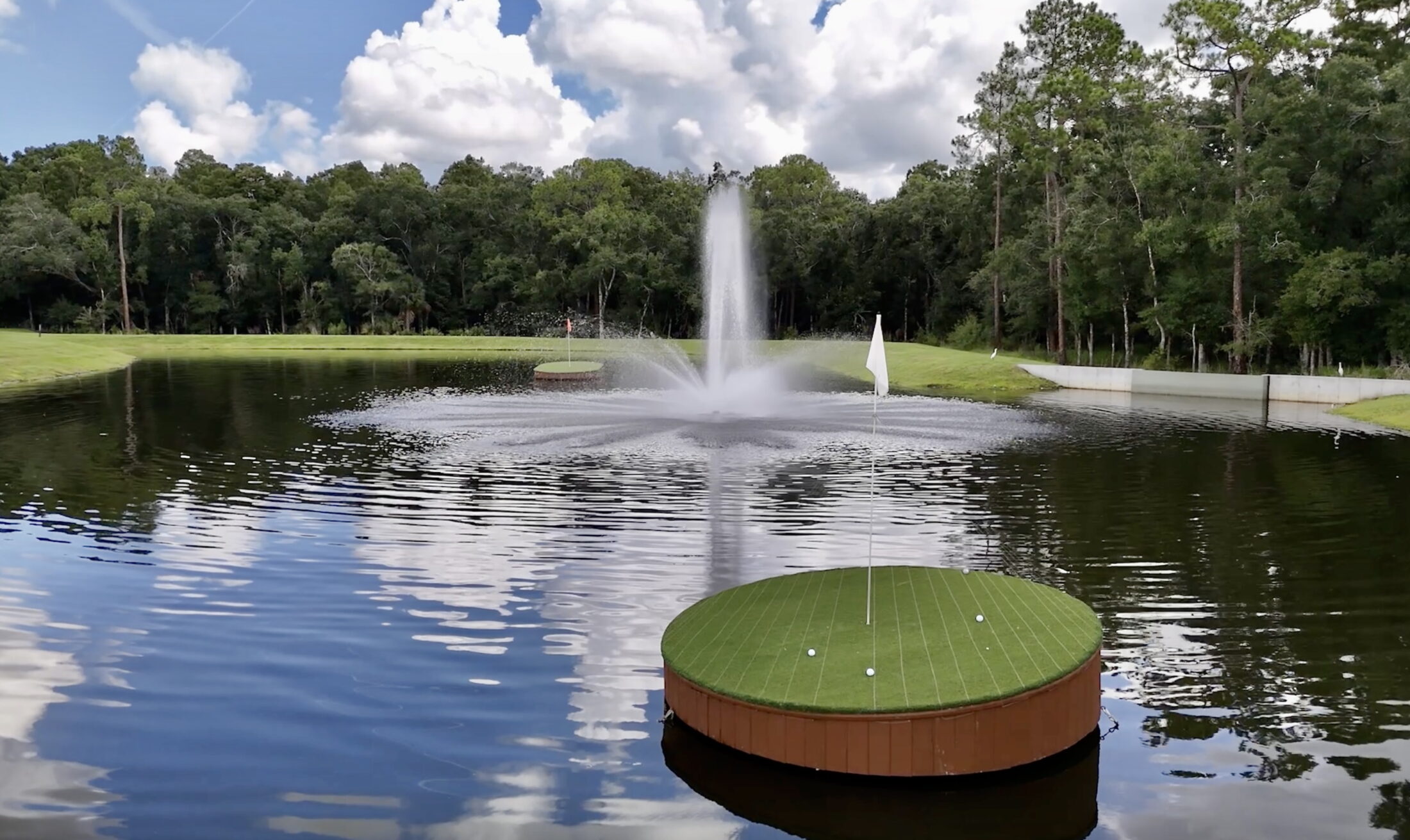 Golf green floating in a pond with a sprinkler behind it